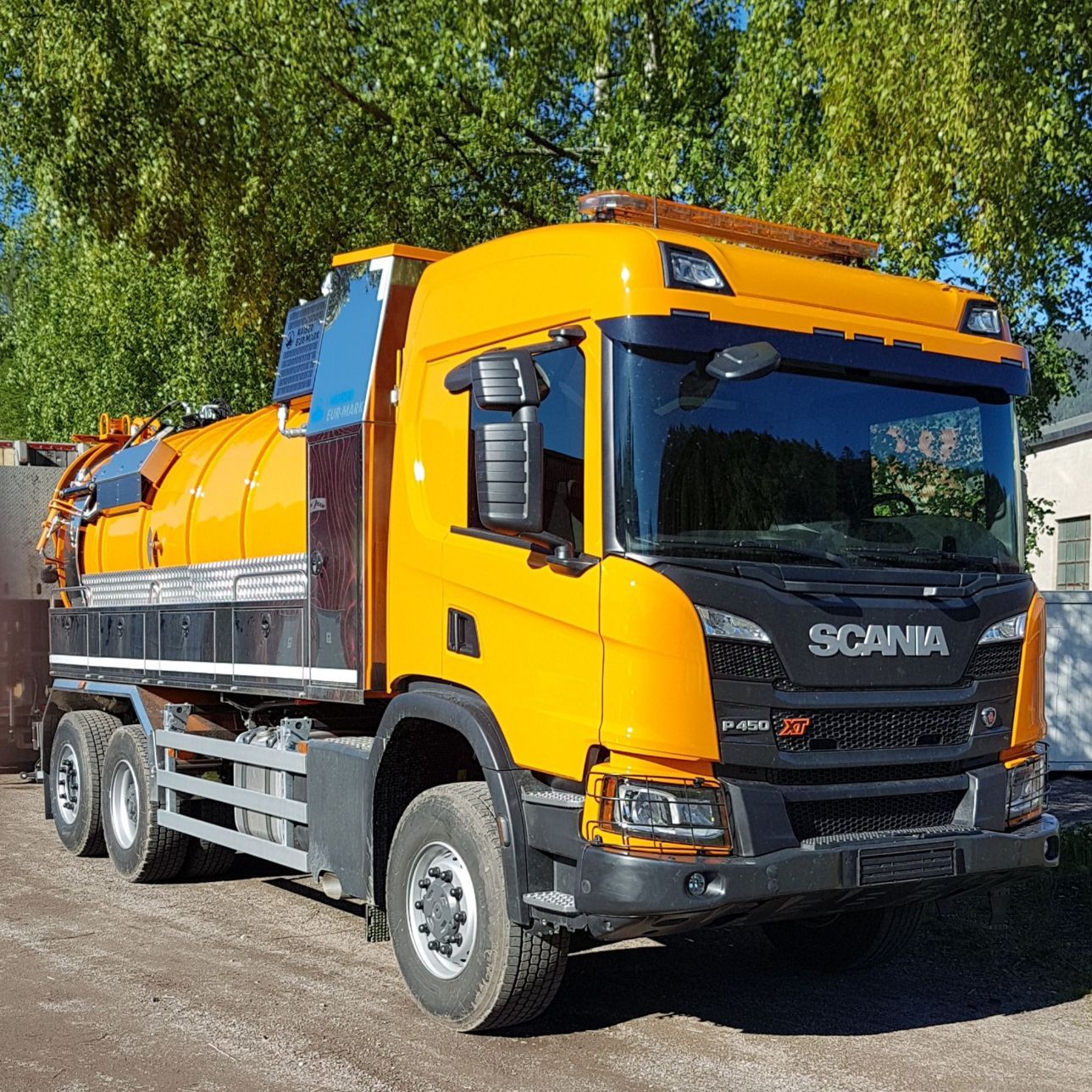 en oransje scania lastebil som står foran et tre under en blå himmel