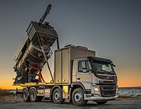 en lastebil som har hele lasteplanet hevet for å helle ut det som er oppi planet foran en solnedgang på en bakke med frost
