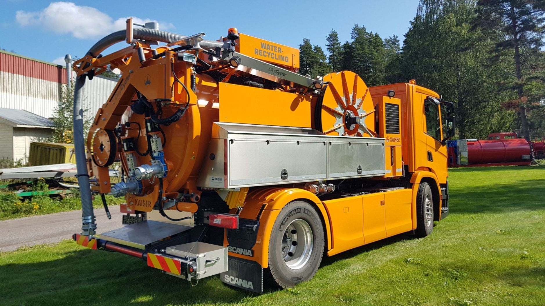 en oransje tankbil med et rør som går ned fra toppen av bilen og ned baksiden som står på en gress plen på en dag med blå himmel