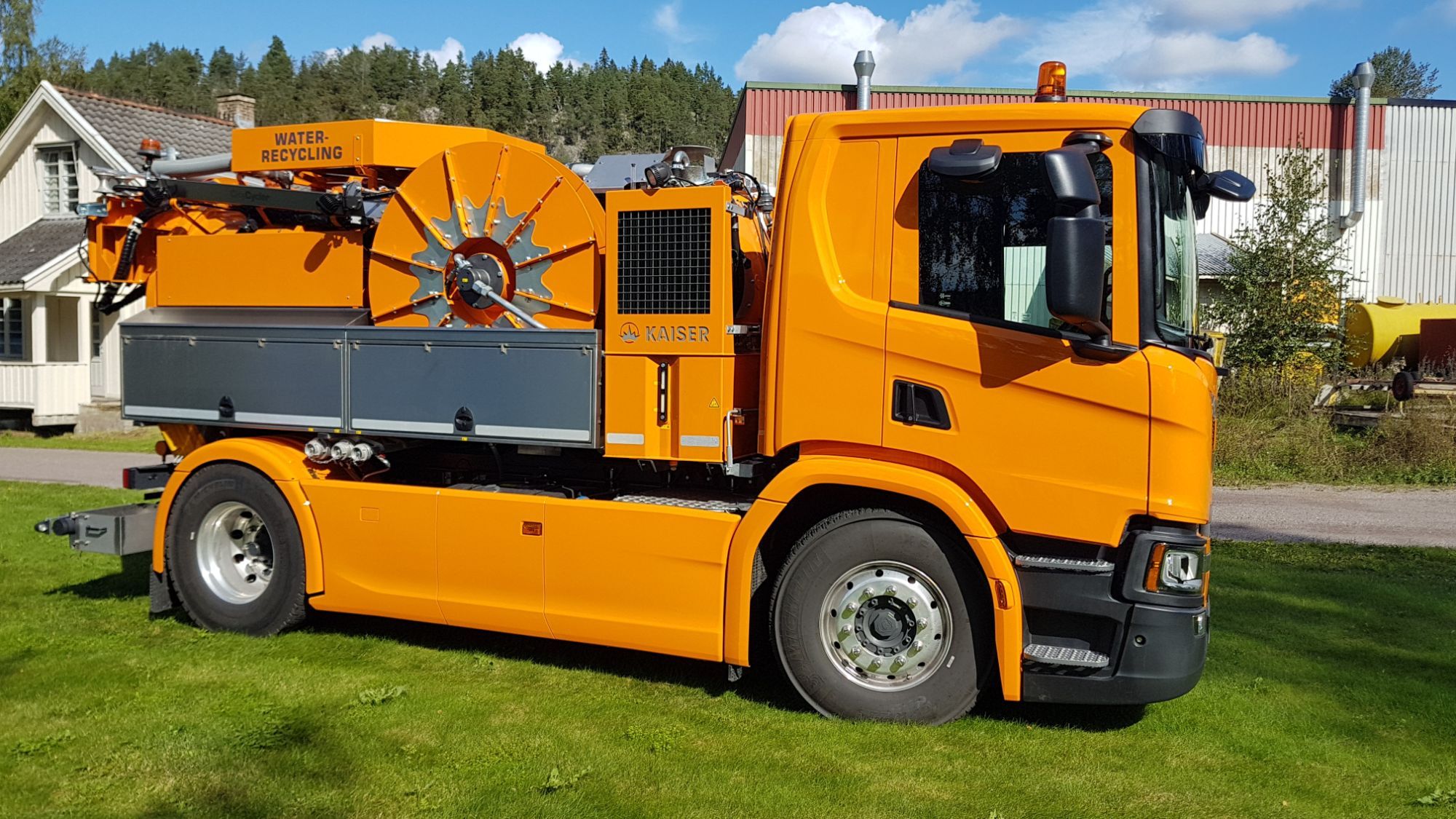 en oransje tankbil med et rør som går ned fra toppen av bilen og ned baksiden som står på en gress plen på en dag med blå himmel